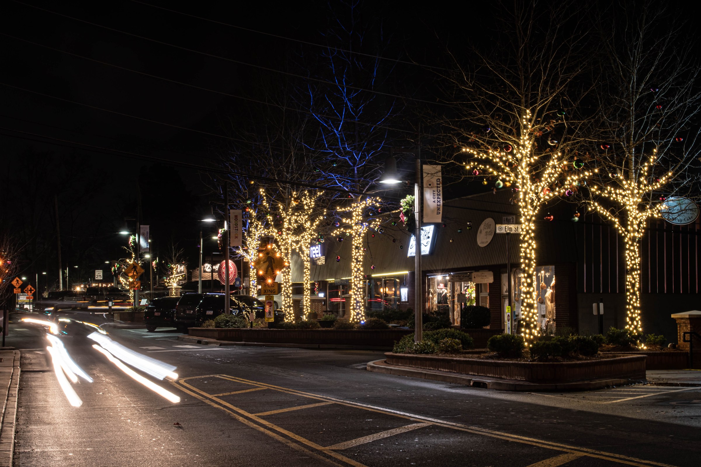 Downtown intersection at night with wrapped street trees and lit storefronts