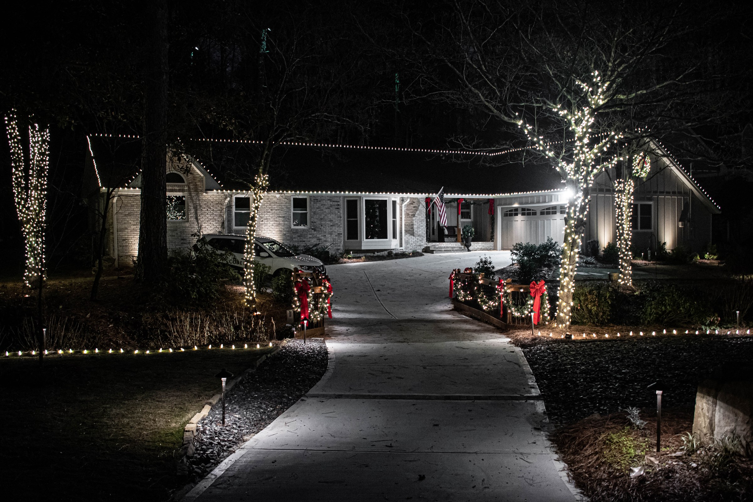 Wrapped trees and a lit span across a driveway at night