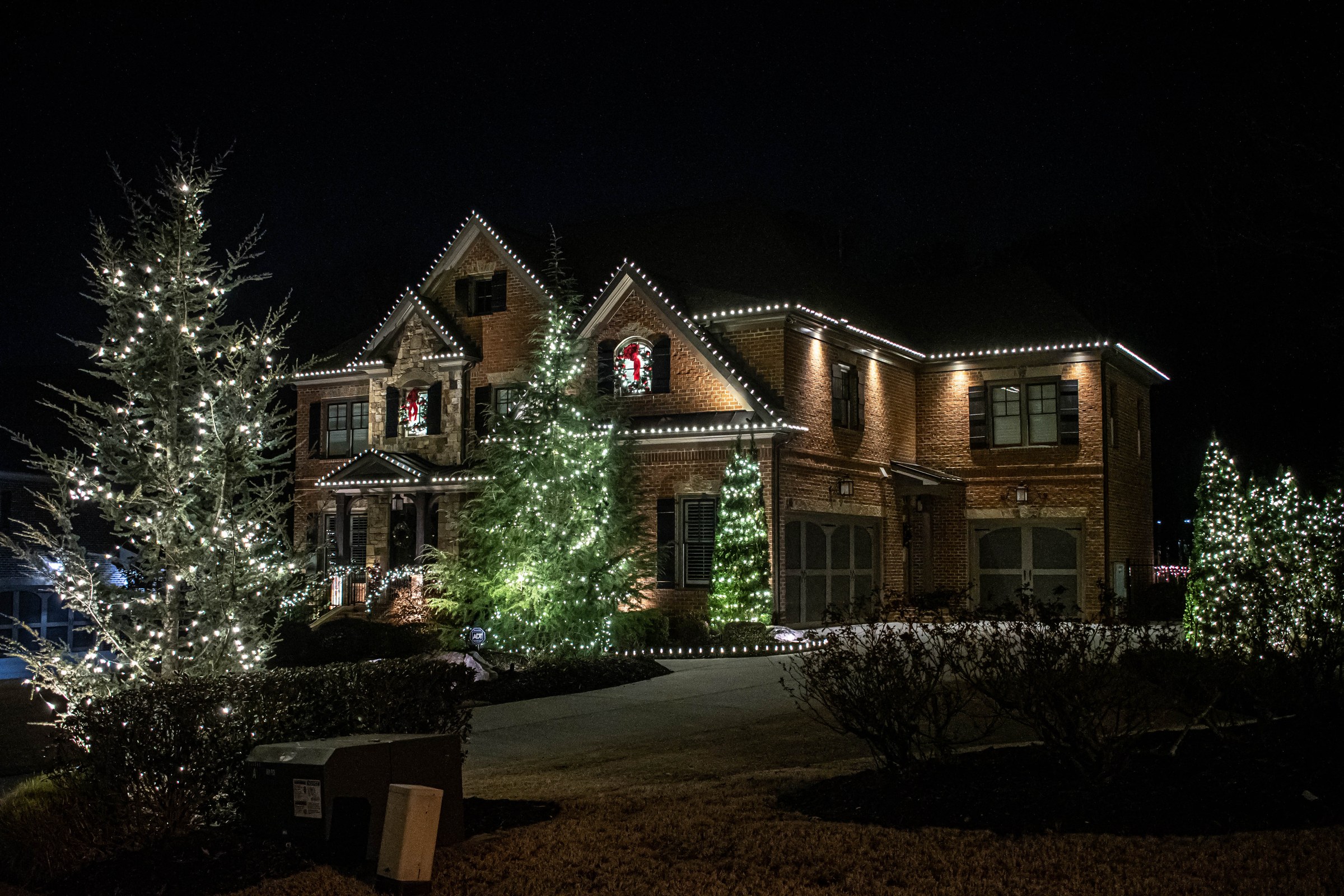 Brick home with lit evergreens, wreaths and a full front elevation