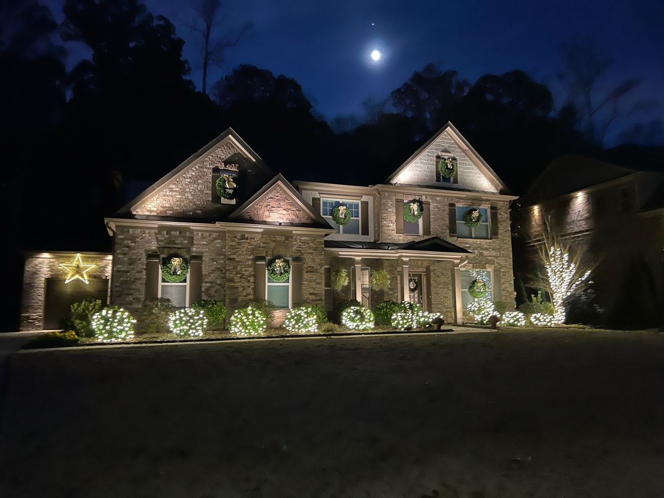 Fresh wreaths and gold ribbon, gable to garage, with lit shrubs